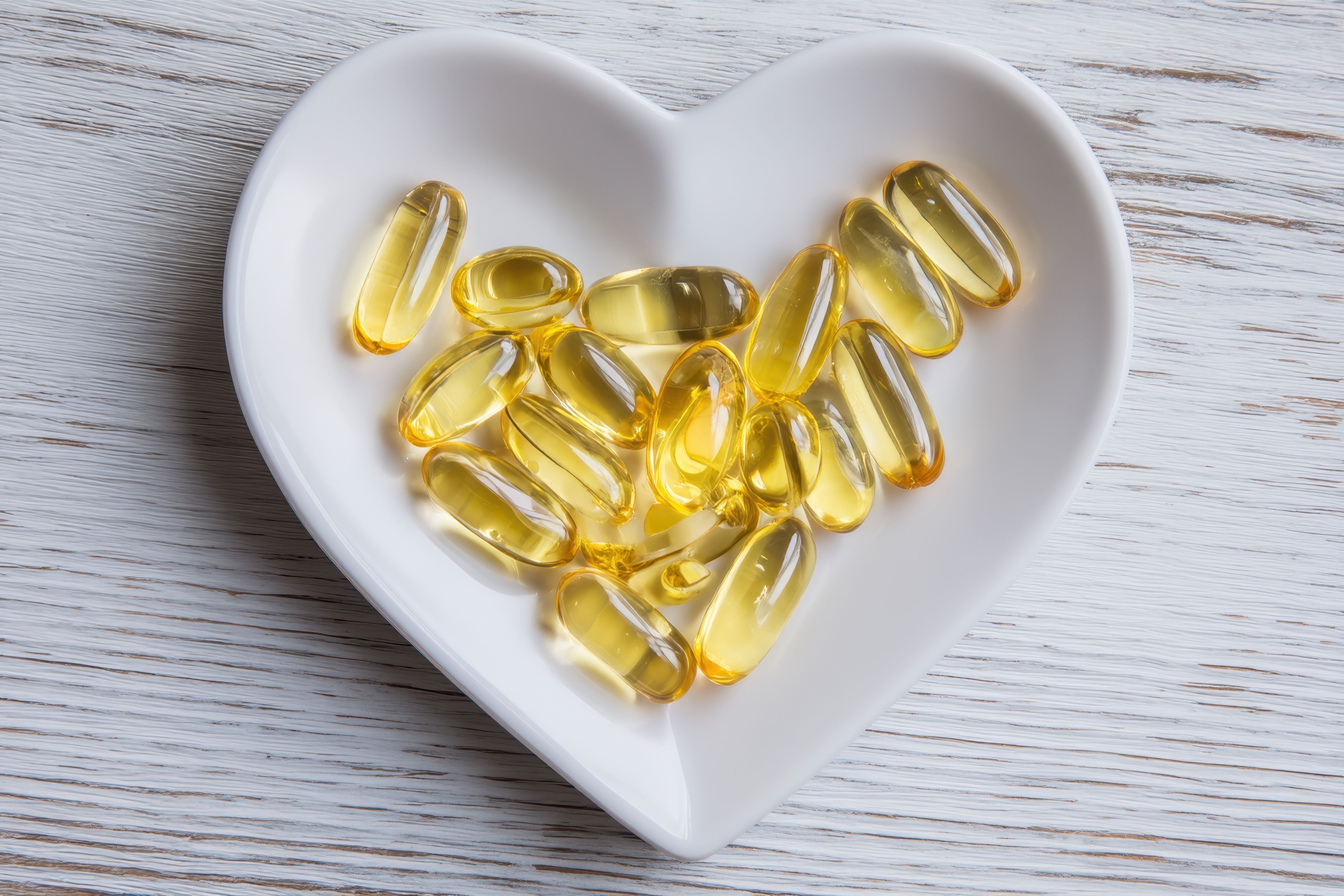 Heart-shaped dish of golden softgel capsules on whitewashed wood